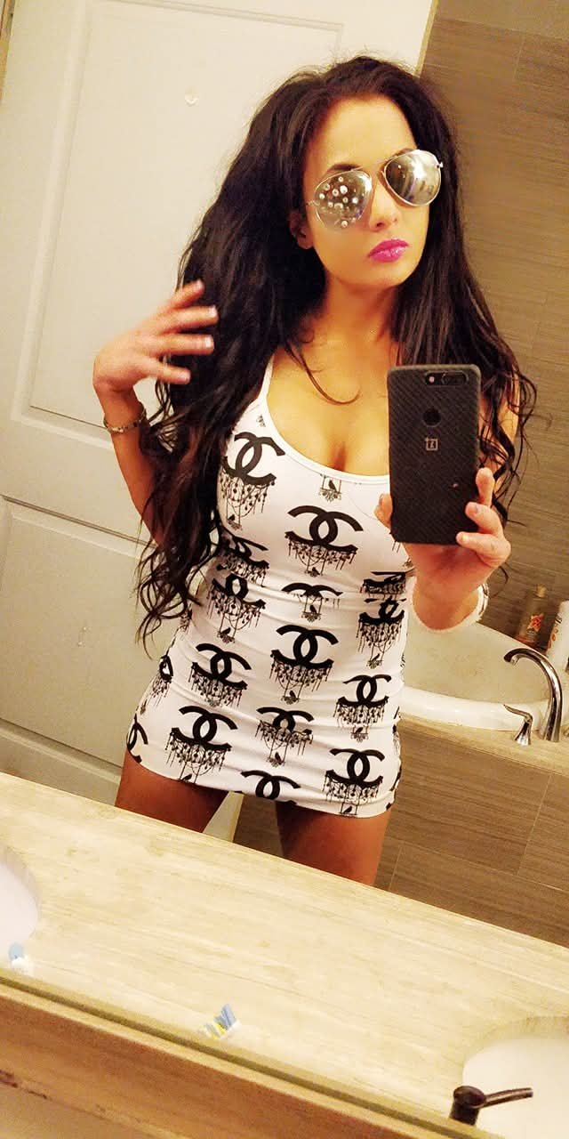Jennifer Jorgensen Ahmed in a white logo dress and mirrored sunglasses taking a bathroom mirror selfie