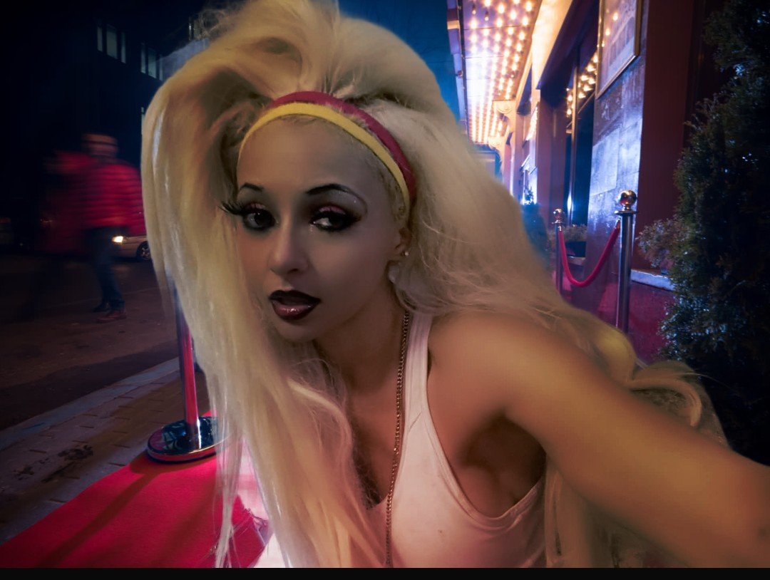 Jennifer Jorgensen Ahmed on the red carpet outside a theater marquee at night, wearing a pink and yellow headband